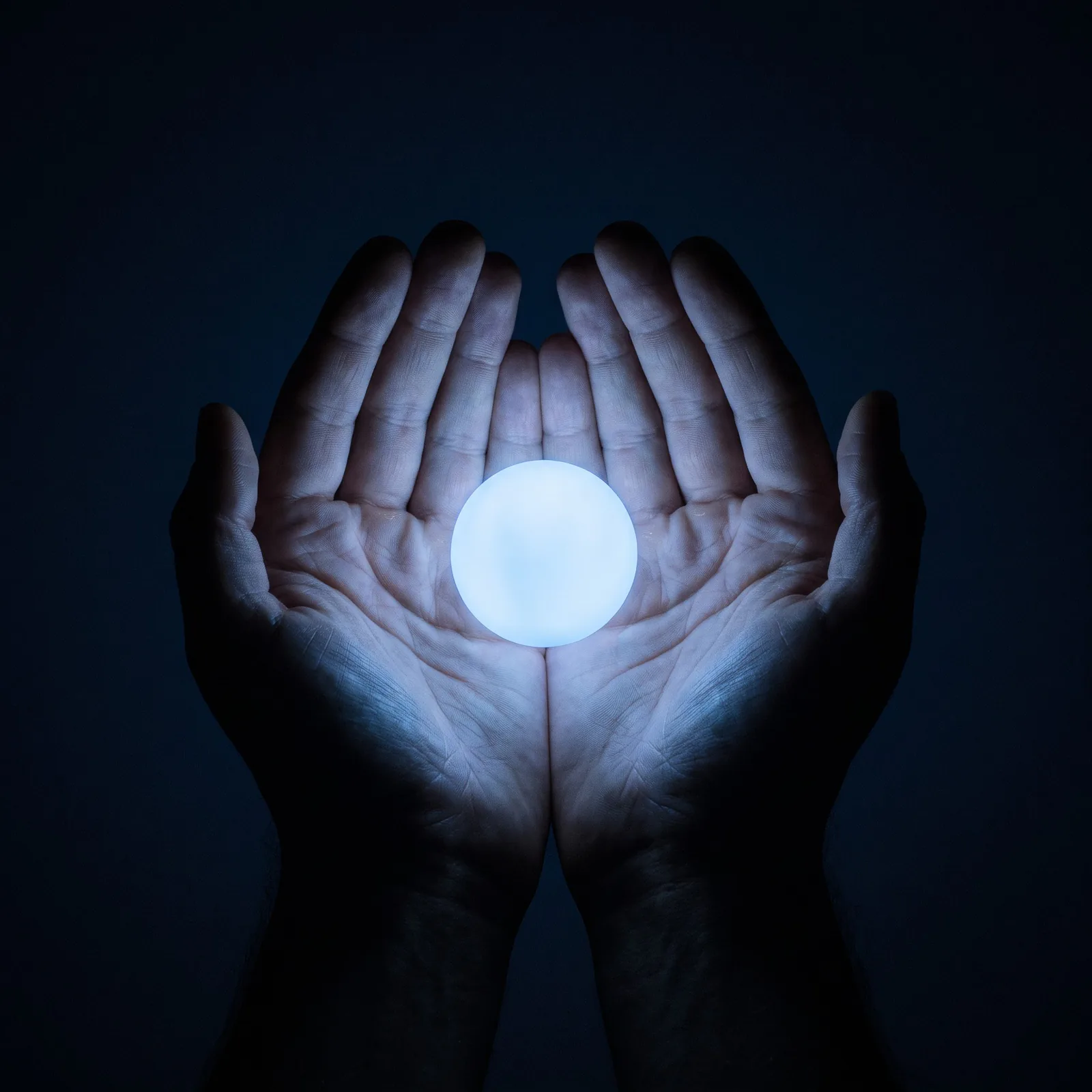 Two cupped hands offering a sphere of blue light.